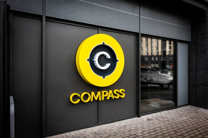 The outside of the building. A black wall, with a door on the right. On the wall is the word COMPASS in big yellow lettering.