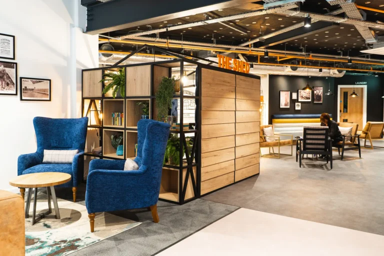 A social area inside Altura House. There are a few comfy blue chairs and shelving. In the background is another seating area with a sofa