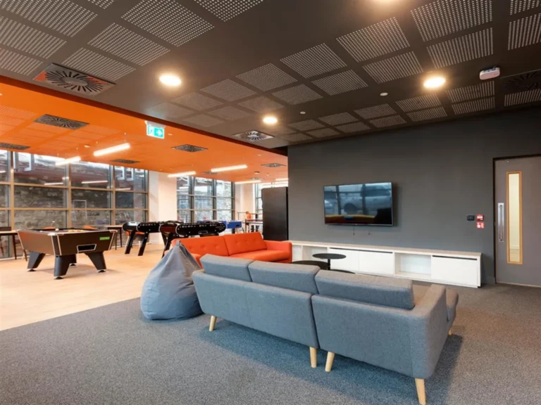 A social area in Brickworks. In the foreground there are a couple of sofas facing a large TV. In the background there are pool tables.