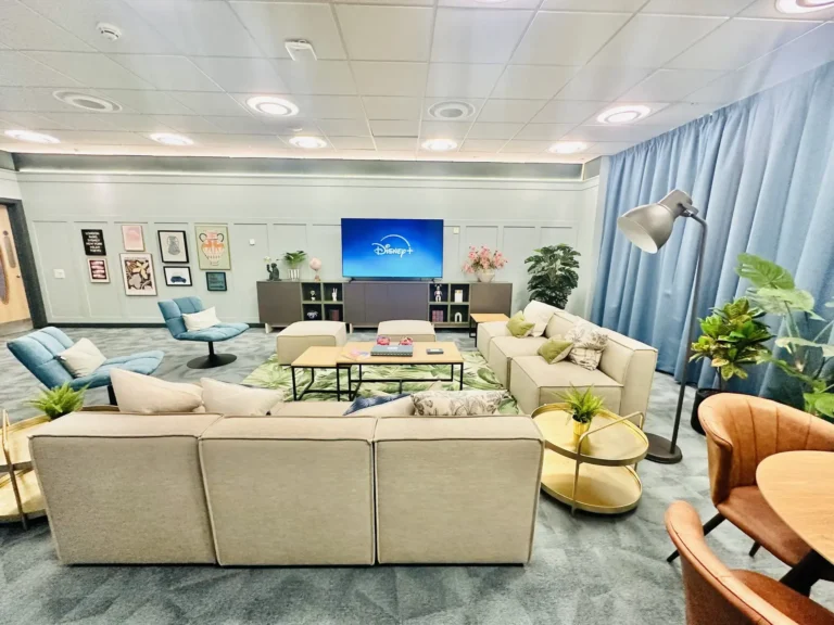 A shared living space. There are sofas, comfy chairs. a small table and a large TV