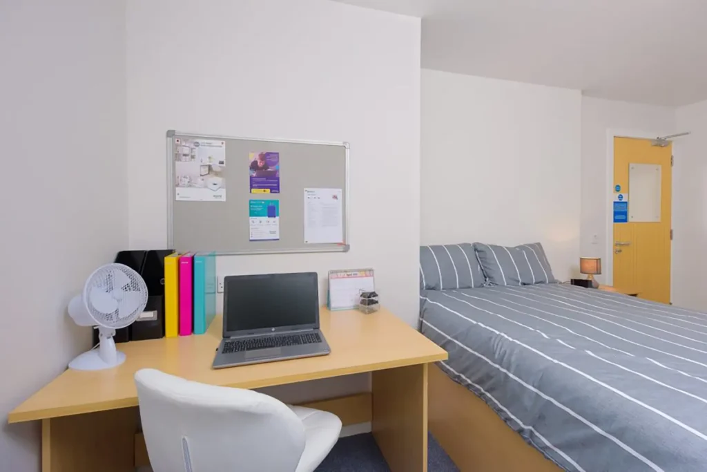 A bedroom at Keiller Court. There is a desk with a laptop on, and a chair for the desk. There is also a good sized bed.