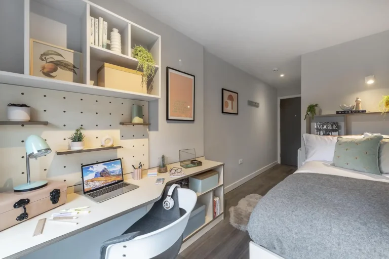 A large student bedroom with a desp and a large bed. The room is spacious and light.