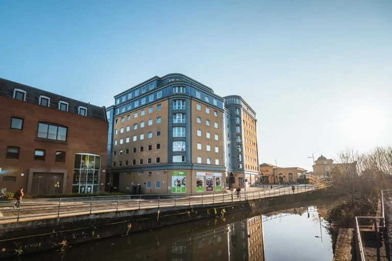 An external photo of The Junxion - student accommodation. It's a large building with nine floors. It is yellow, and set against a blue sky.