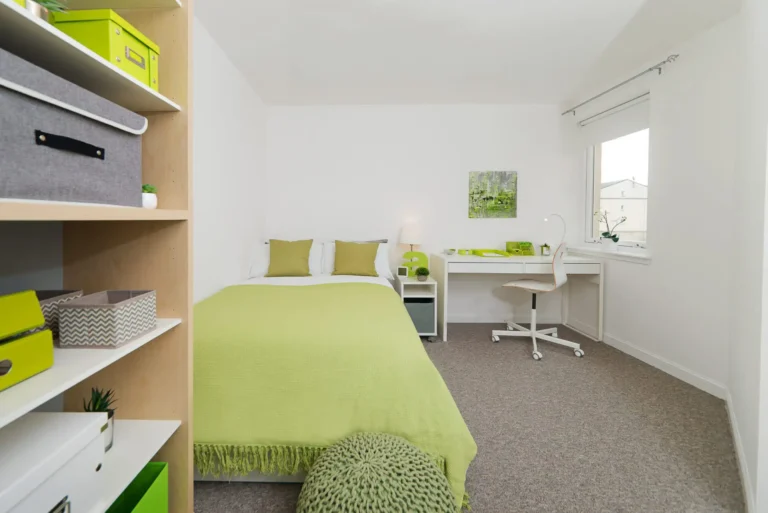 A large bedroom. The furnishings are a nice bright green. There is a 3/4 size bed, a work desk with chair and storage space.