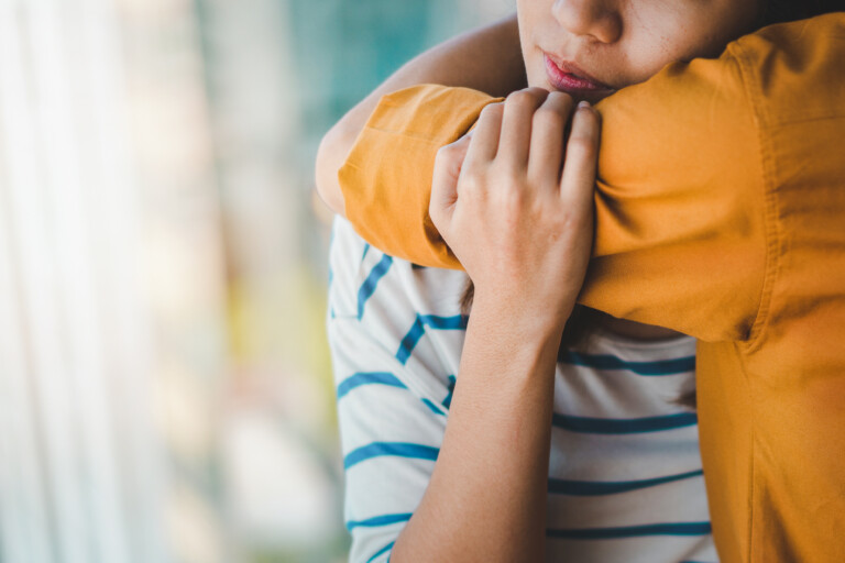 Student hugging a peer in a time of need. Student is wearing a white and blue stripy top and the person they are hugging is wearing and orange shirt.