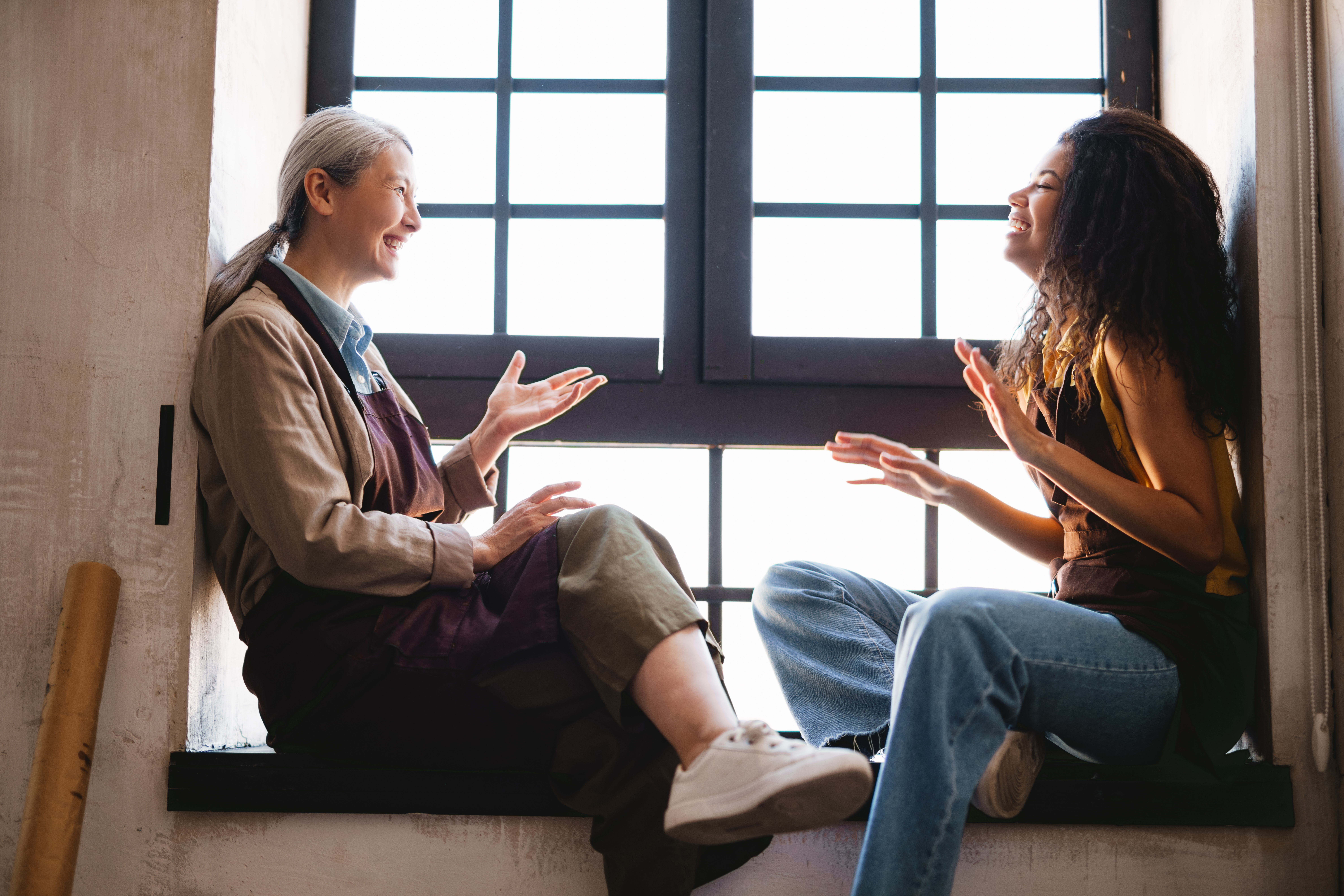 student talking with a teacher, expressing feelings sat on some steps in front of a window